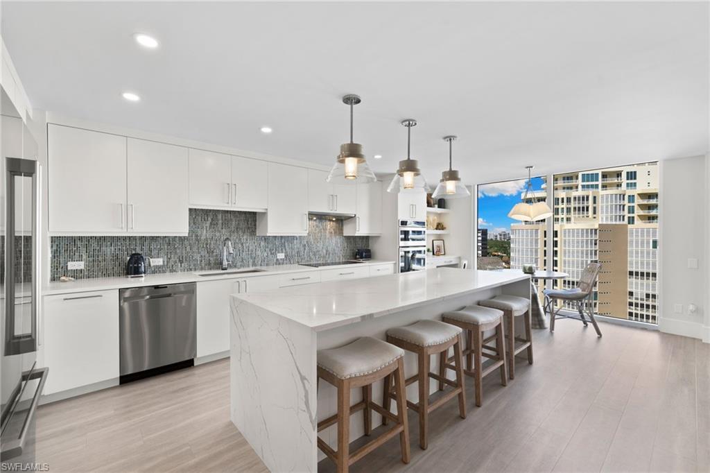 Image 2: Kitchen with white cabinetry, tasteful backsplash, hanging light fixtures, appliances with stainless steel finishes, and light wood-style floors