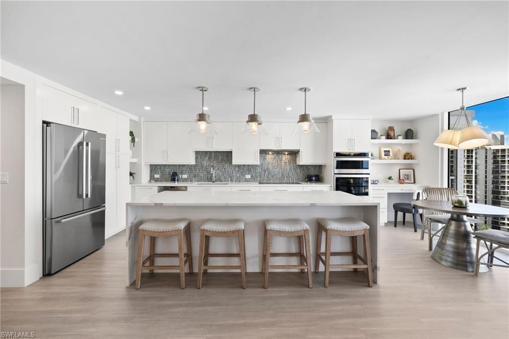 Image 3: Kitchen featuring white cabinetry, stainless steel appliances, light stone countertops, a kitchen breakfast bar, and backsplash