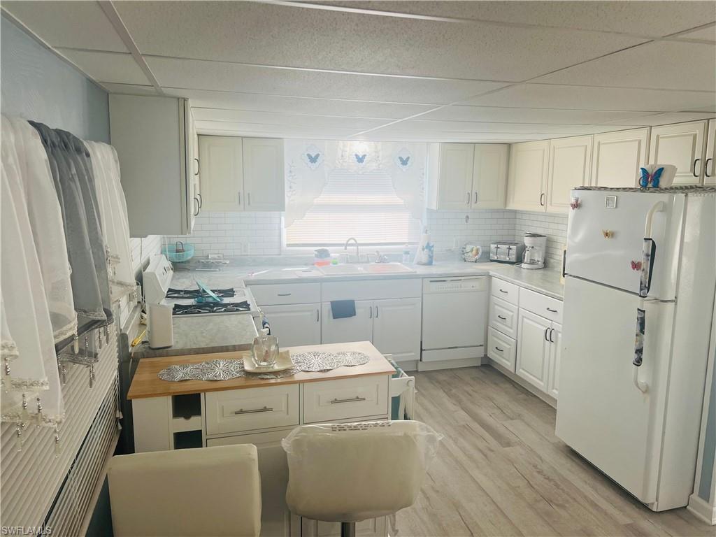 Image 3: Kitchen with white appliances, white cabinets, light wood finished floors, light countertops, and a paneled ceiling