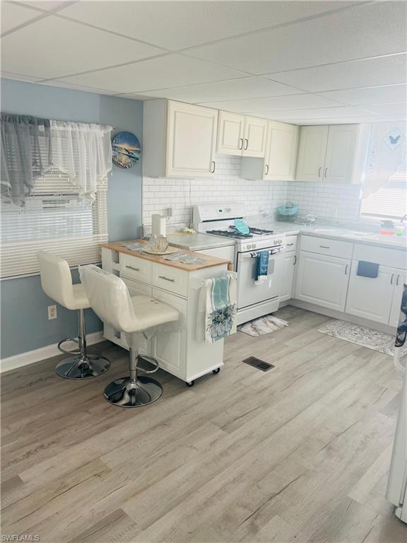 Image 4: Kitchen with light countertops, white range with gas cooktop, white cabinetry, light wood-style flooring, and backsplash