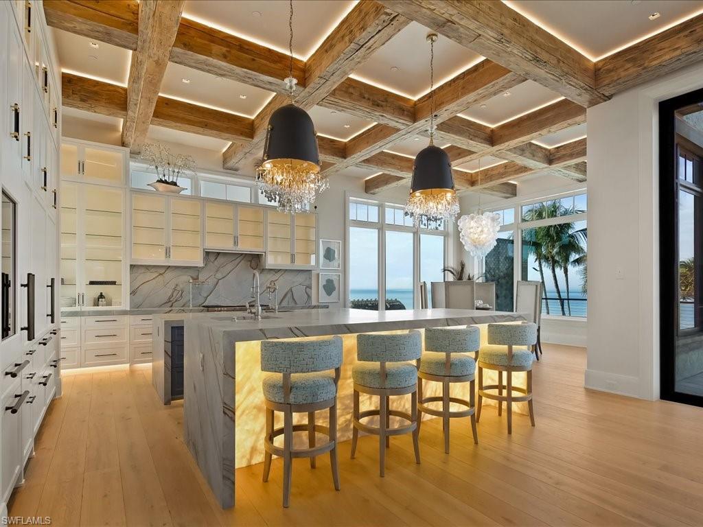 Image 4: Kitchen featuring a breakfast bar, hanging light fixtures, light stone countertops, beam ceiling, and coffered ceiling