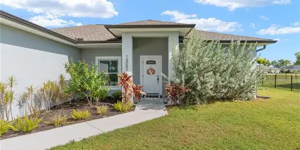 Image 2: View of exterior entry featuring a shingled roof and stucco siding