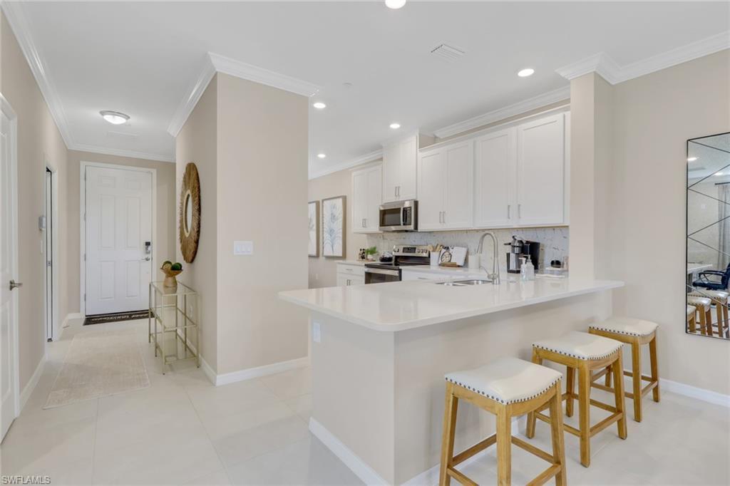 Image 4: Kitchen with ornamental molding, tasteful backsplash, white cabinetry, stainless steel appliances, and a kitchen breakfast bar