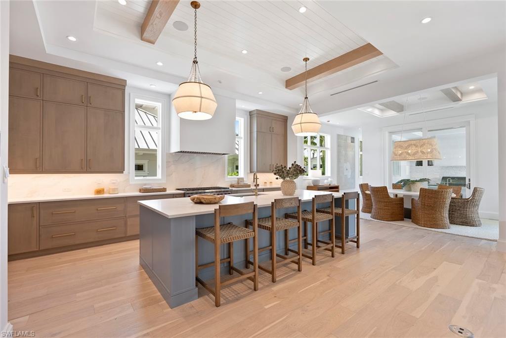 Image 4: Kitchen featuring hanging light fixtures, a kitchen bar, an island with sink, light wood-style floors, and beamed ceiling