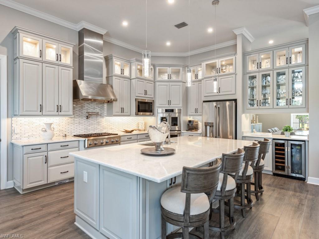 Image 4: Kitchen featuring ornamental molding, a breakfast bar area, wine cooler, light stone counters, and appliances with stainless steel finishes