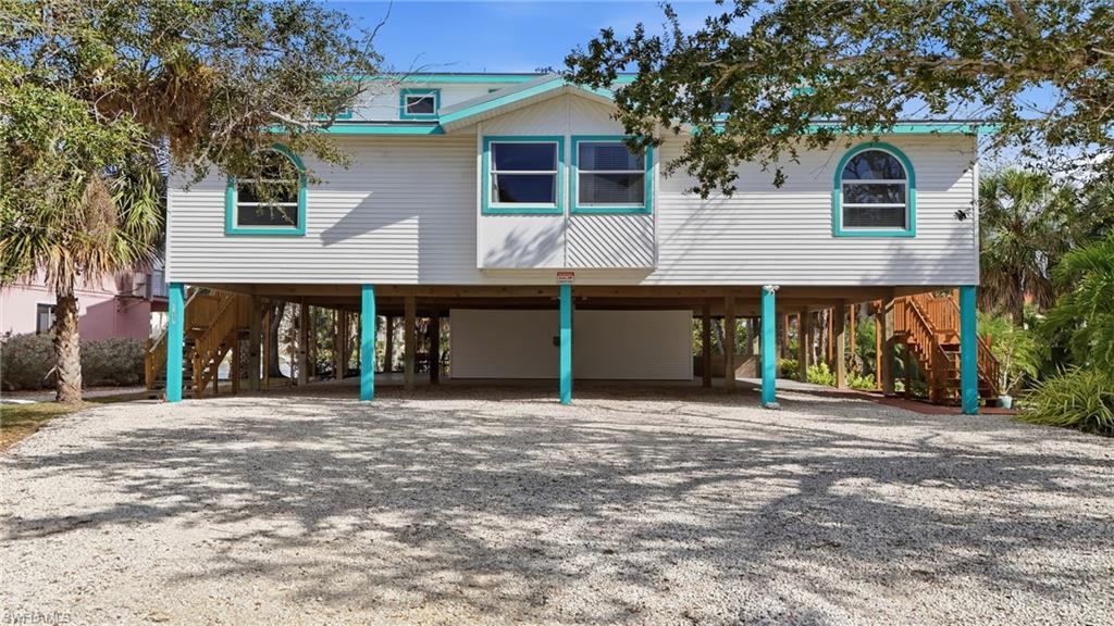 Image 1: Coastal inspired home featuring a carport, stairs, and gravel driveway - Virtually Edited Image