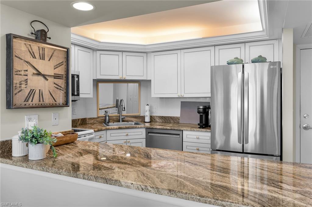 Image 4: Kitchen with stainless steel appliances, dark stone countertops, and white cabinetry