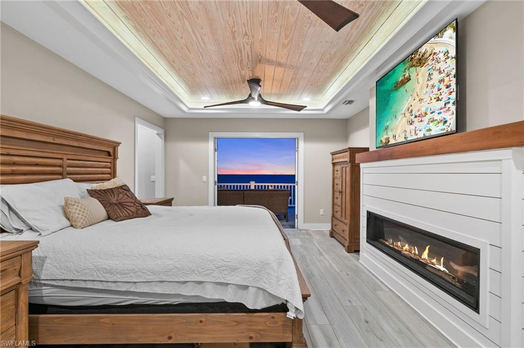 Image 4: Primary bedroom featuring recessed wood ceiling, french doors to third floor balcony,  light grey finished floors, 2  ceiling fans, remote control propane fire place.