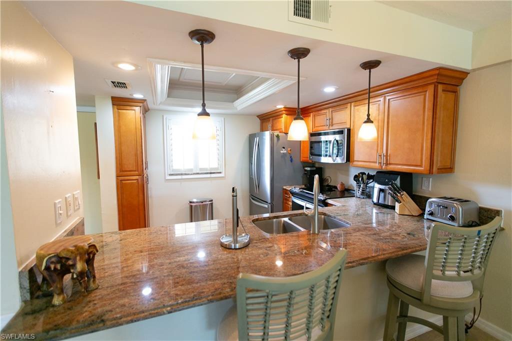 Image 2: Kitchen featuring a raised ceiling, a peninsula, ornamental molding, stainless steel microwave, and a kitchen bar