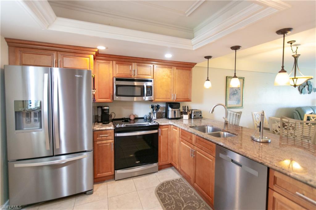 Image 3: Kitchen with stainless steel appliances, light stone counters, a raised ceiling, ornamental molding, and brown cabinetry