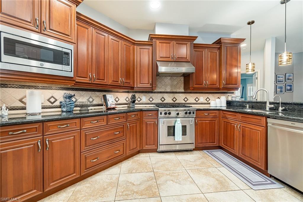 Image 3: Kitchen featuring stainless steel appliances, hanging light fixtures, dark stone countertops, under cabinet range hood, and light tile patterned floors
