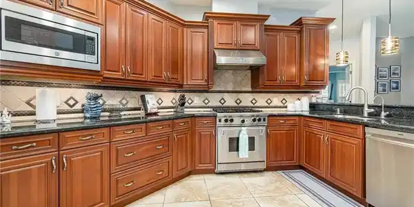 Image 3: Kitchen featuring stainless steel appliances, hanging light fixtures, dark stone countertops, under cabinet range hood, and light tile patterned floors