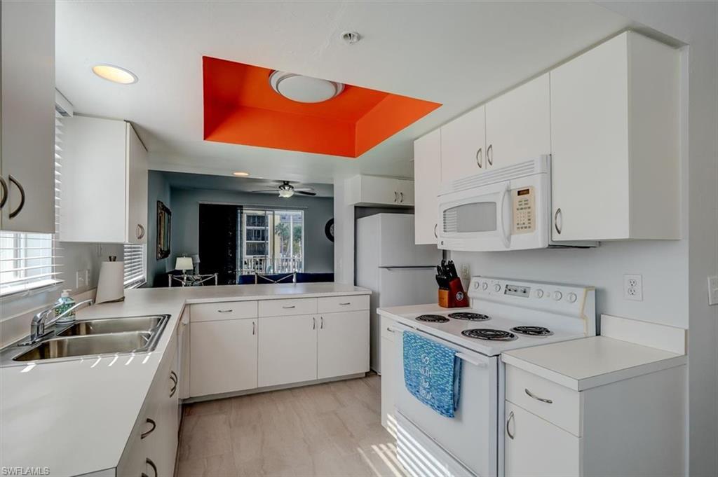 Image 2: Kitchen featuring a tray ceiling, sink, white cabinets, and white appliances. Note open view towards living area