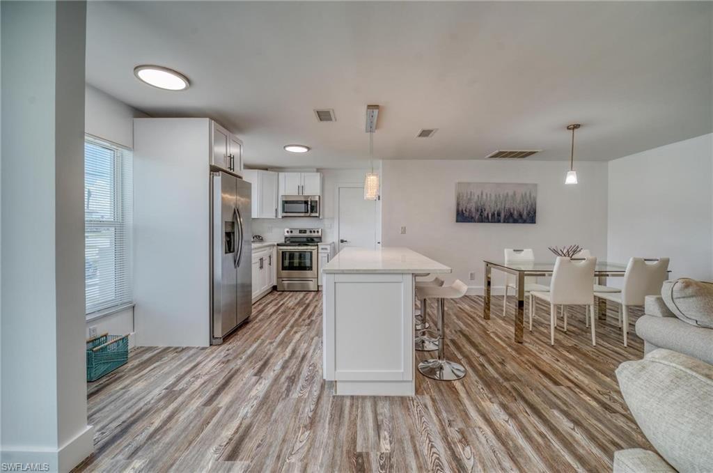 Image 2: Kitchen featuring stainless steel appliances, a breakfast bar area, light wood-style floors, light countertops, and white cabinetry