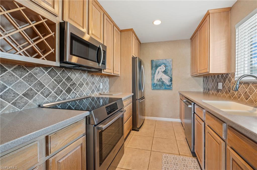 Image 3: Kitchen featuring stainless steel appliances, light tile patterned flooring, decorative backsplash, light countertops, and recessed lighting