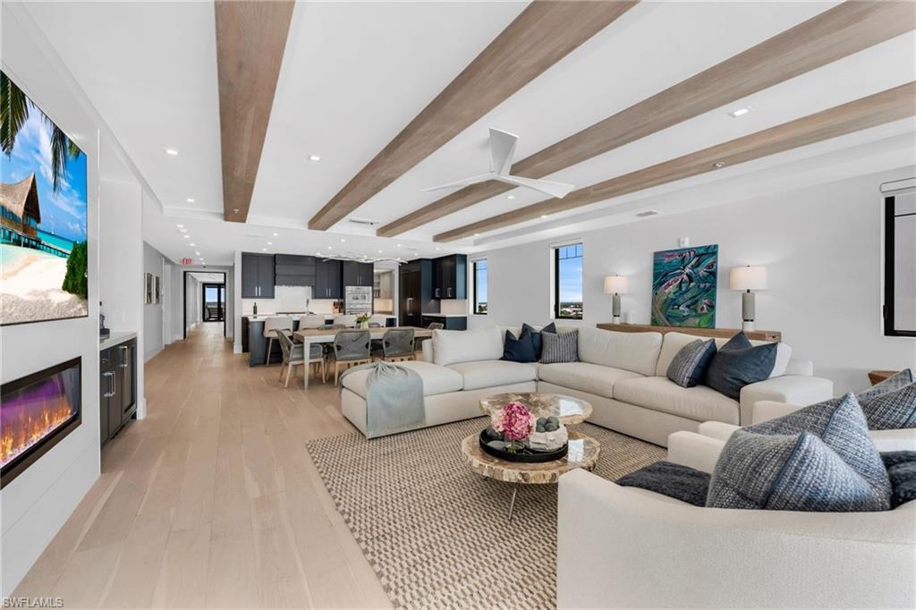 Image 3: Living area featuring beam ceiling, a glass covered fireplace, light wood-type flooring, and recessed lighting