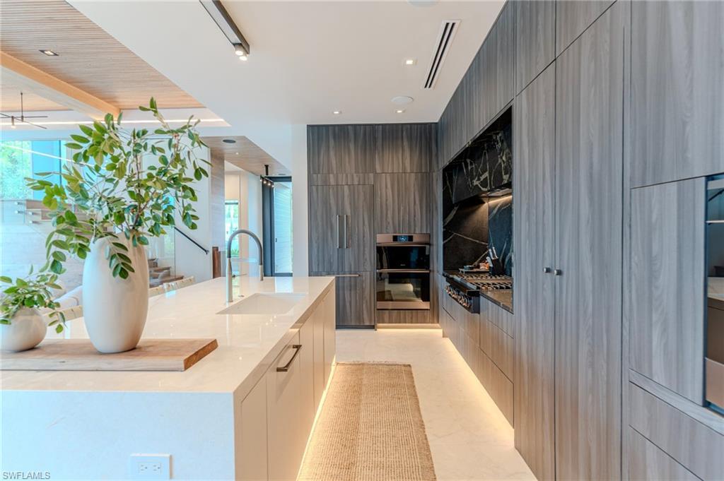 Image 4: Kitchen with light stone counters, modern cabinets, appliances with stainless steel finishes, a center island with sink, and recessed lighting