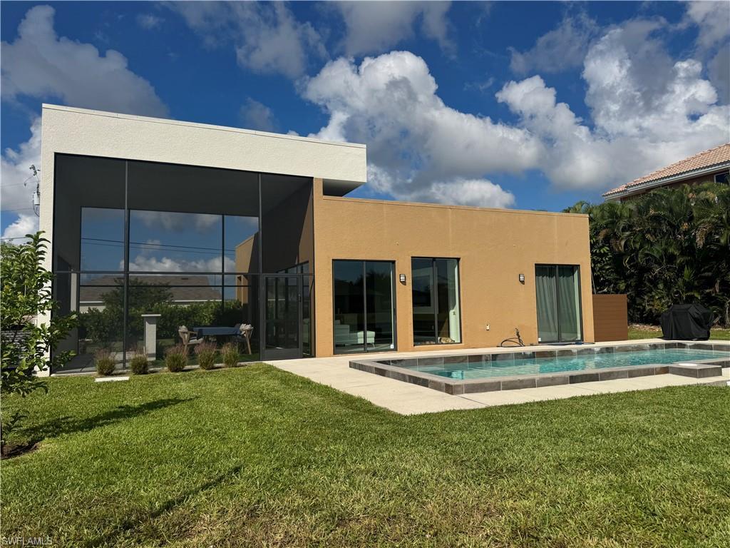 Image 2: Rear view of property featuring a yard, a sunroom, an outdoor pool, and stucco siding