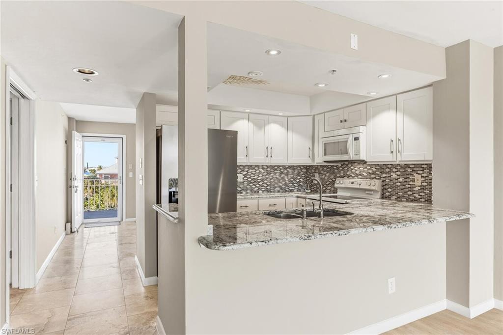 Image 4: Kitchen featuring white appliances, white cabinetry, light stone countertops, tasteful backsplash, and recessed lighting