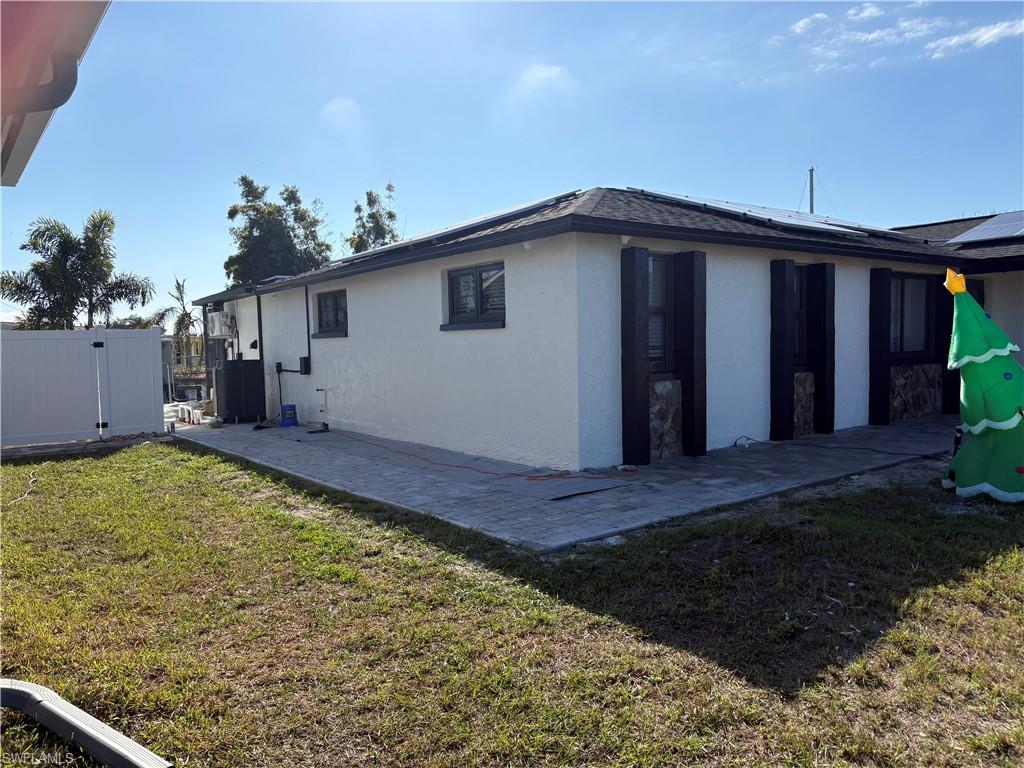 Image 3: View of side of home with solar panels, stucco siding, a patio area, and a gate