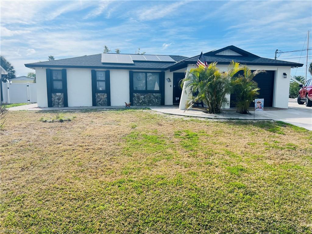 Image 4: Single story home with roof mounted solar panels, a gate, stucco siding, and a front lawn