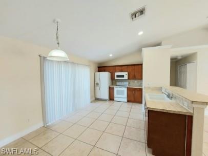 Image 3: Kitchen with white appliances, pendant lighting, lofted ceiling, light tile patterned flooring, and tile countertops