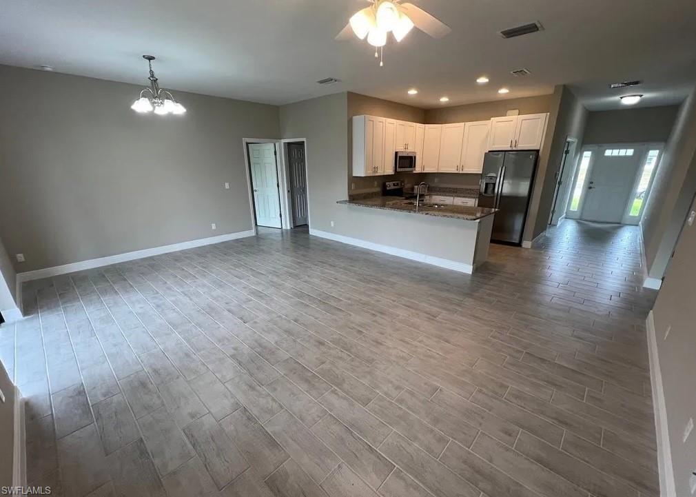 Image 2: Kitchen featuring open floor plan, fridge with ice dispenser, dark stone countertops, white cabinetry, and recessed lighting