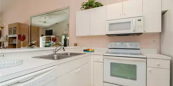 Image 2: Kitchen with white cabinets, white appliances, lofted ceiling, and sink