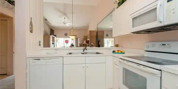 Image 4: Kitchen with white appliances, ceiling fan, sink, decorative light fixtures, and white cabinetry