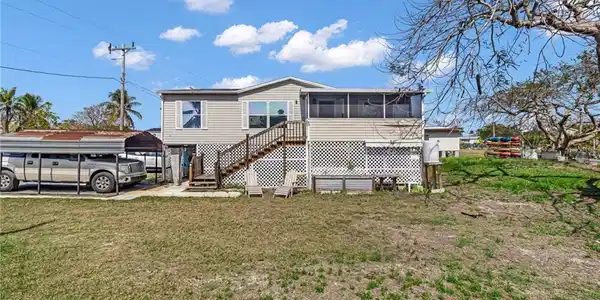 Image 2: Back of property featuring stairs, a detached carport, a lawn, and a sunroom
