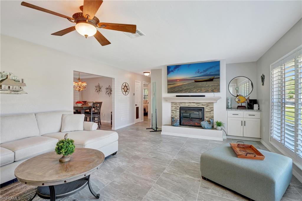 Image 2: Living room with baseboards, a fireplace, visible vents, and ceiling fan with notable chandelier