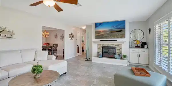 Image 2: Living room with baseboards, a fireplace, visible vents, and ceiling fan with notable chandelier