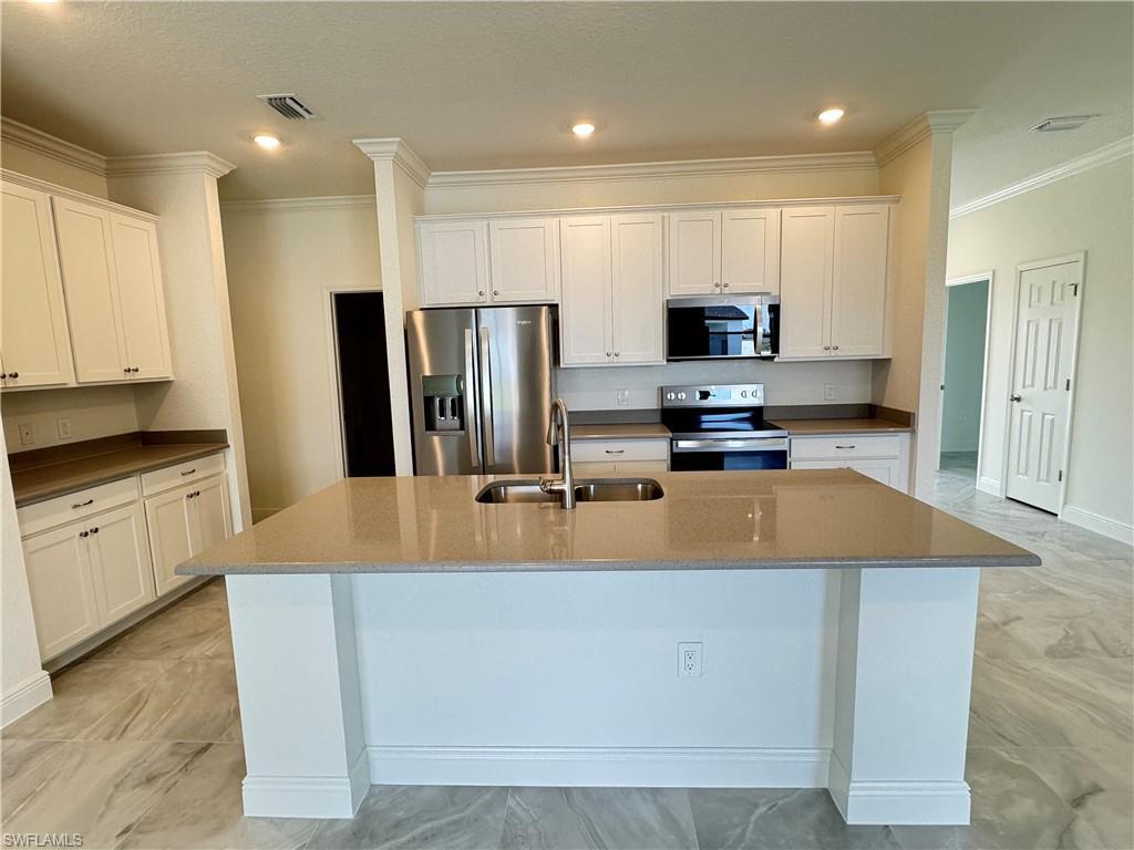 Image 2: Kitchen with appliances with stainless steel finishes, a sink, light marble finish floors, an island with sink, and ornamental molding