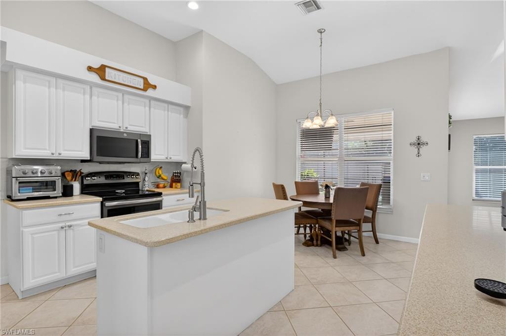 Image 4: Kitchen with white cabinetry, stainless steel appliances, light tile patterned flooring, and lofted ceiling