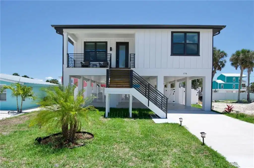 Image 1: View of front of home with a carport, stairway, concrete driveway, a front lawn, and board and batten siding - Virtually Edited Image