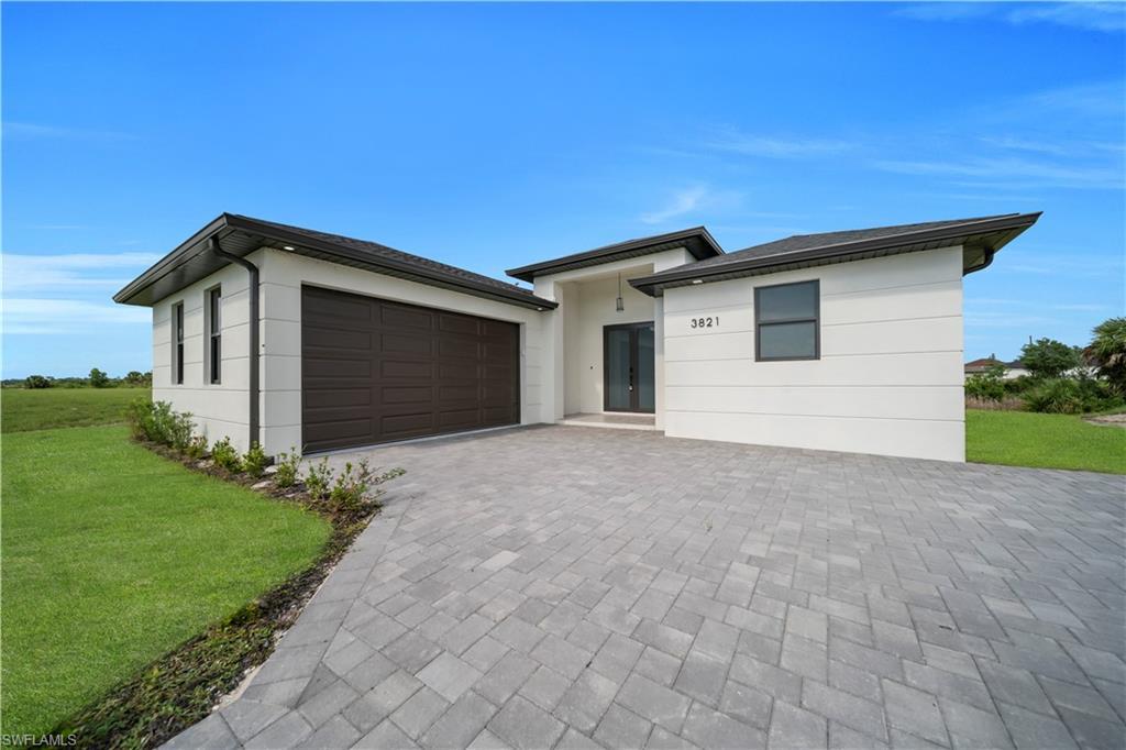Image 2: Prairie-style home featuring a front lawn, decorative driveway, an attached garage, and stucco siding