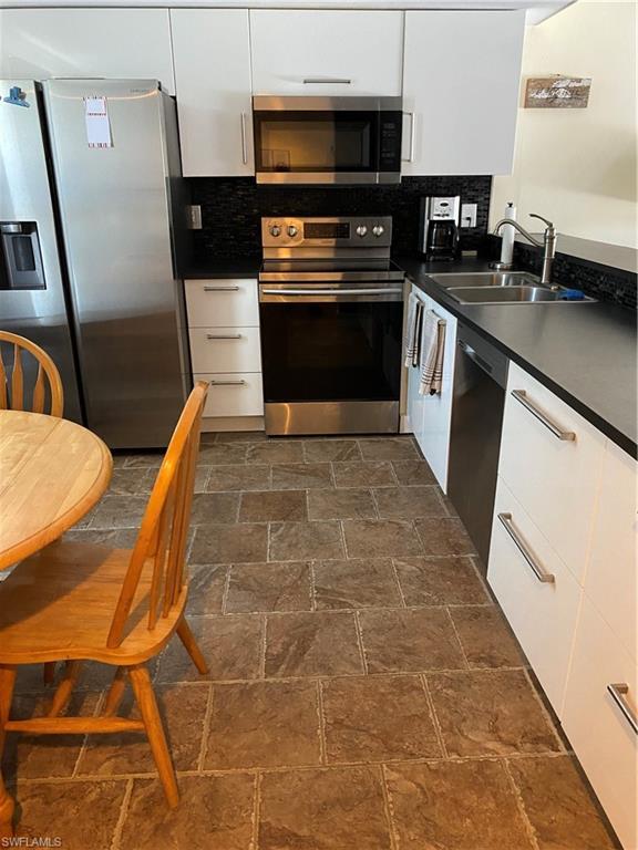 Image 4: Kitchen featuring appliances with stainless steel finishes, dark countertops, white cabinetry, backsplash, and modern cabinets