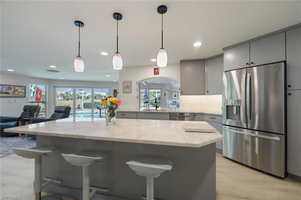 Image 2: Kitchen with gray cabinets, stainless steel appliances, open floor plan, a kitchen breakfast bar, and hanging light fixtures