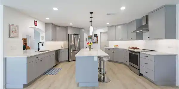 Image 3: Kitchen featuring gray cabinetry, a kitchen breakfast bar, appliances with stainless steel finishes, wall chimney exhaust hood, and hanging light fixtures