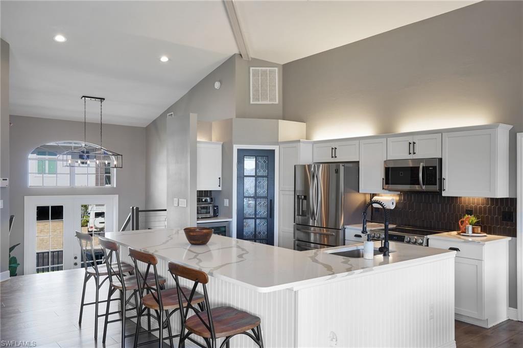 Image 2: Kitchen with high vaulted ceiling, beamed ceiling, white cabinets, stainless steel appliances, and tasteful backsplash