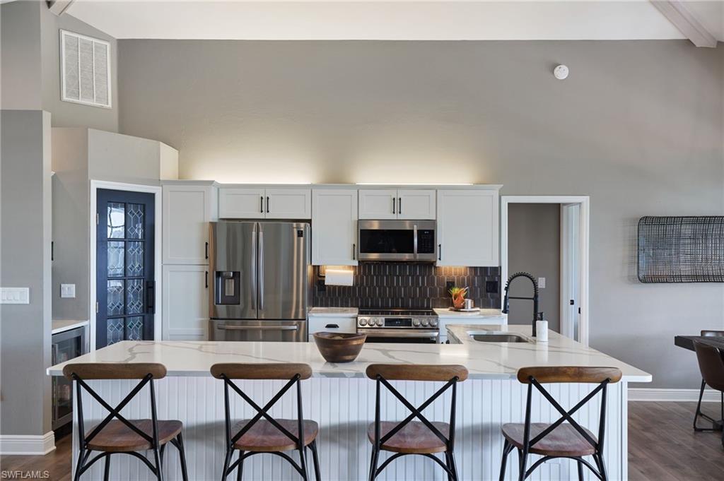 Image 4: Kitchen with appliances with stainless steel finishes, an island with sink, white cabinetry, beamed ceiling, and light stone counters