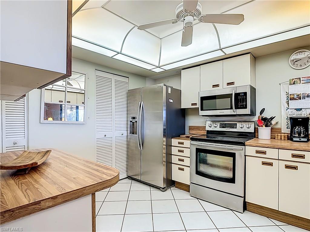 Image 3: Kitchen with stainless steel appliances, white cabinetry, a ceiling fan, wooden counters, and light tile patterned floors