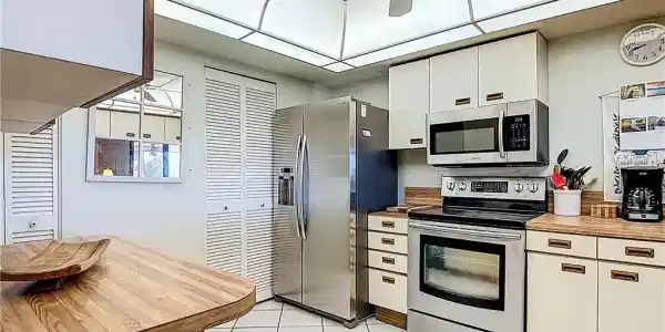 Image 3: Kitchen with stainless steel appliances, white cabinetry, a ceiling fan, wooden counters, and light tile patterned floors