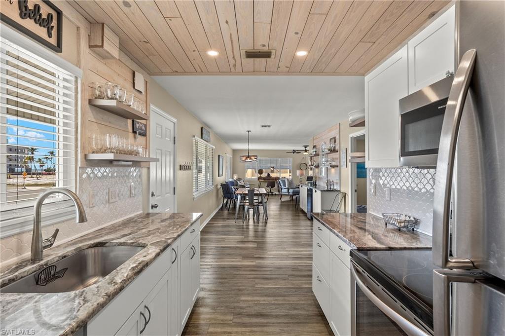 Image 3: Kitchen featuring white cabinets, wooden ceiling, a sink, stainless steel appliances, and backsplash