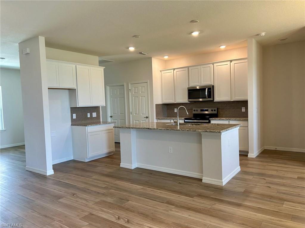 Image 2: Kitchen with appliances with stainless steel finishes, backsplash, light wood-style floors, a kitchen island with sink, and dark stone counters
