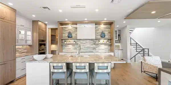 Image 3: Kitchen featuring light stone counters, pendant lighting, open shelves, a center island with sink, and a breakfast bar area