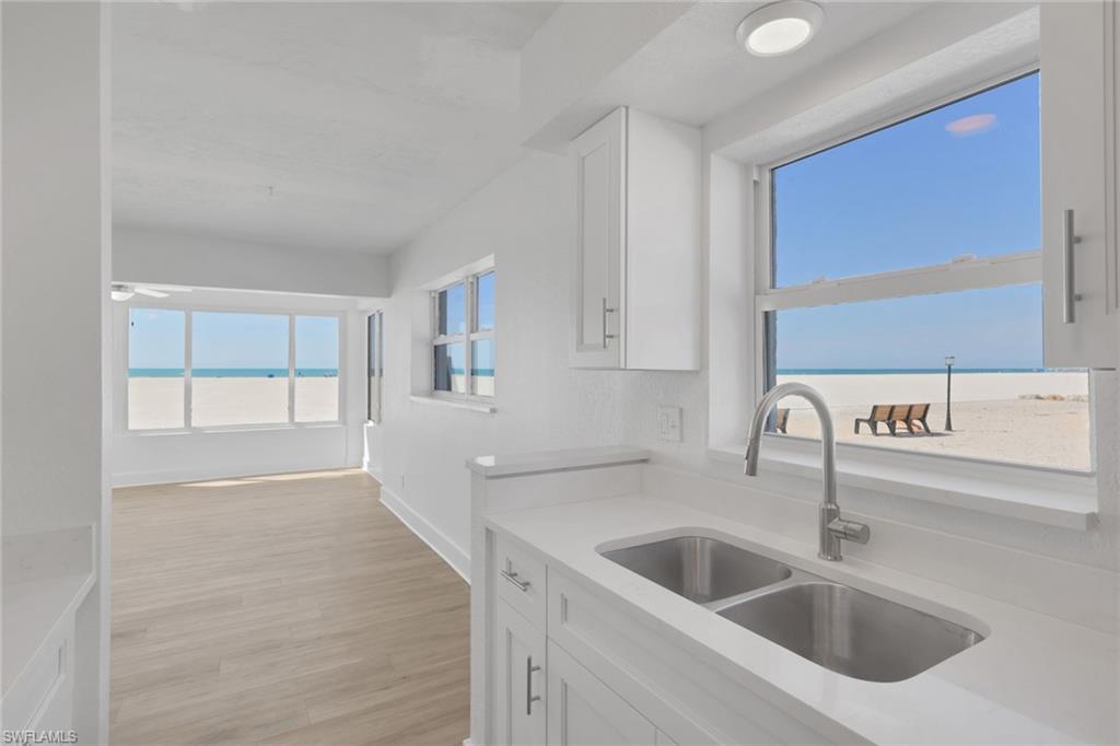 Image 1: Kitchen with white cabinets, light stone counters, light wood-style floors, and a water view