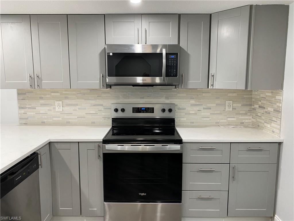 Image 1: Kitchen with gray cabinets, appliances with stainless steel finishes, backsplash, and light stone countertops