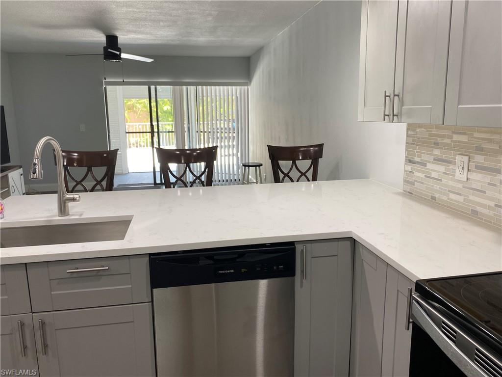 Image 2: Kitchen featuring gray cabinetry, dishwasher, decorative backsplash, and light stone counters