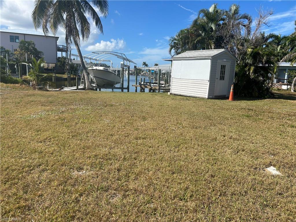 Image 4: View of green lawn featuring boat lift, a dock, a water view, and an outbuilding